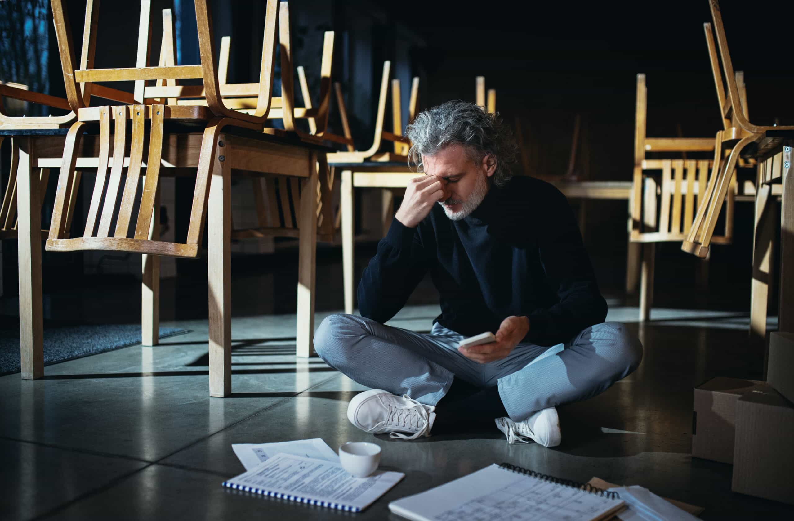 Man sitting on the ground of his restaurant looking stressed reading papers.