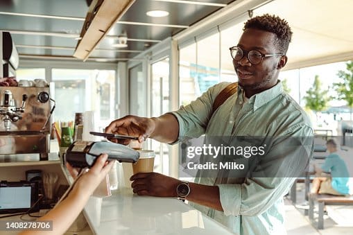 Man paying for a coffee at a cafe counter with his phone.