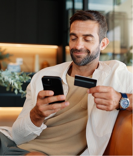 Man sitting and holding a credit card in one hand and his phone in another.