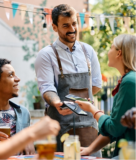 Restaurant waiter smiling at customer who is paying via tap.